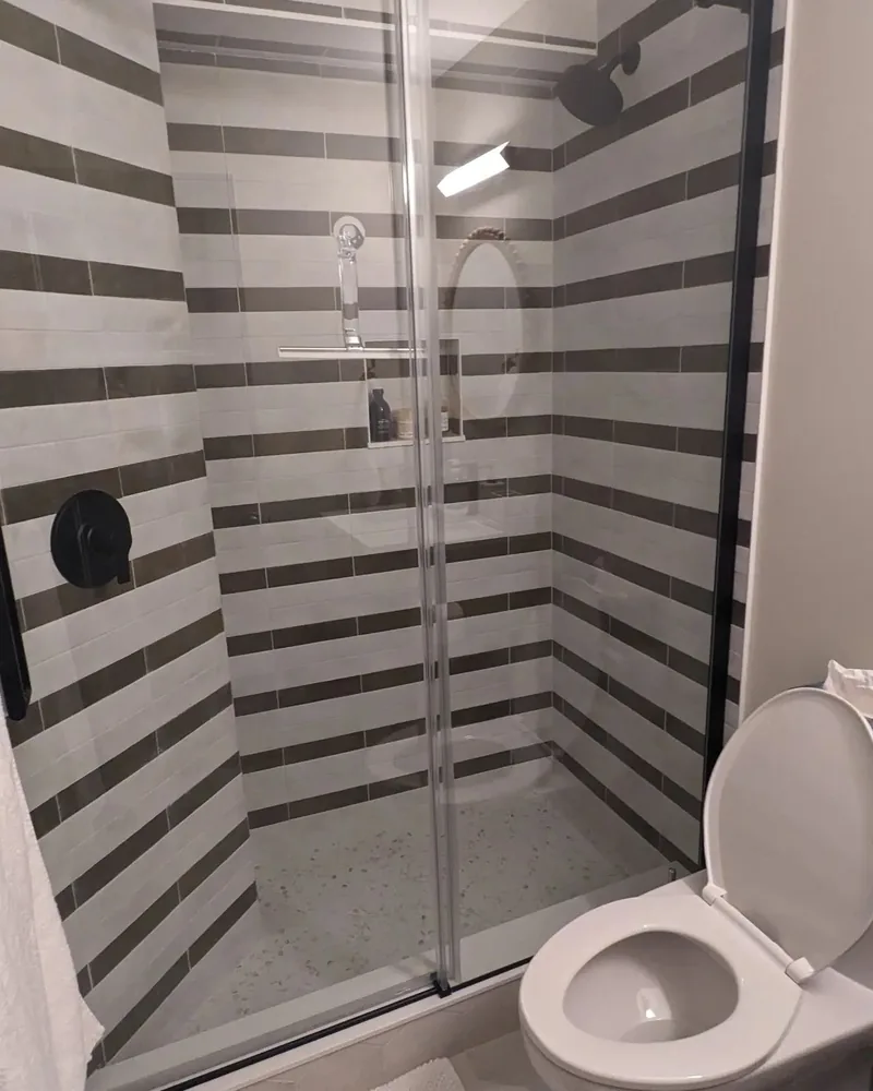 Walk-in shower with alternating grey and white striped tile and glass sliding door