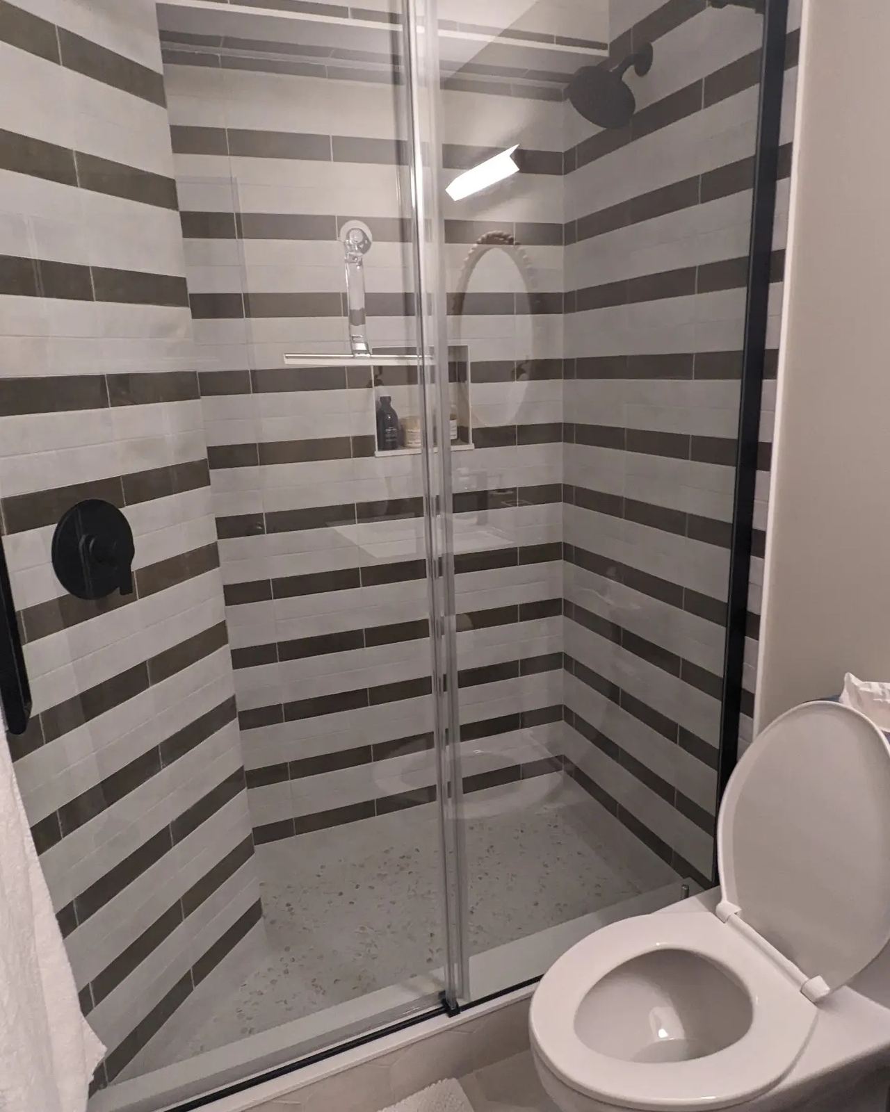 Walk-in shower with striped grey and white tile and glass door