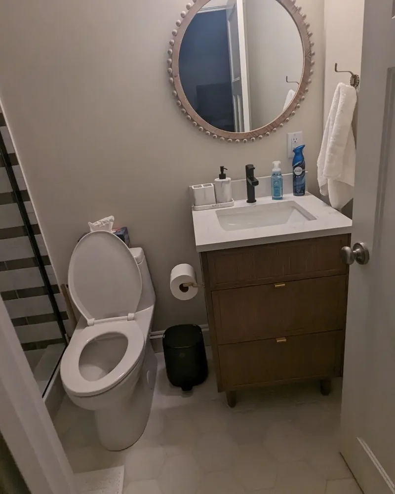 Modern bathroom with wooden vanity, round decorative mirror, and marble-look floor tile