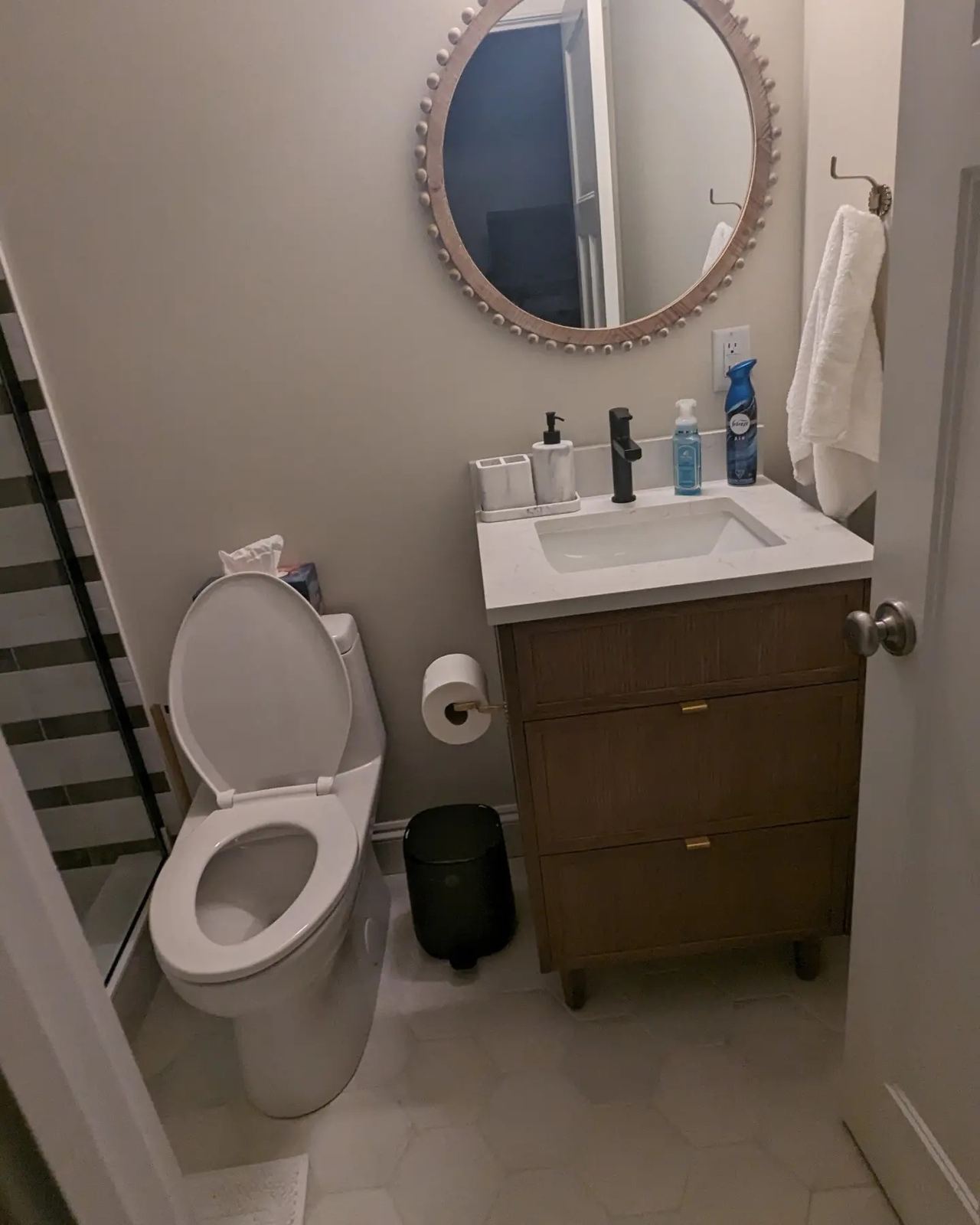 Modern bathroom with wooden vanity, round decorative mirror, and marble-look floor tile