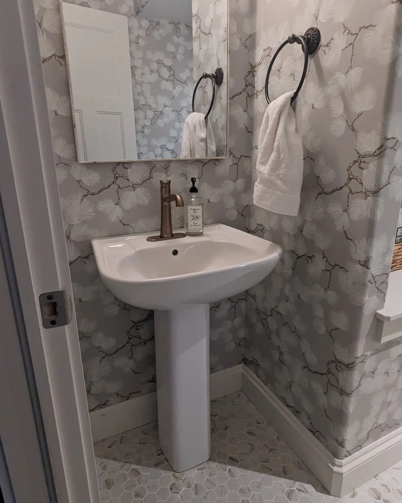 Elegant bathroom renovation with pedestal sink, botanical wallpaper, and hexagonal tile floor