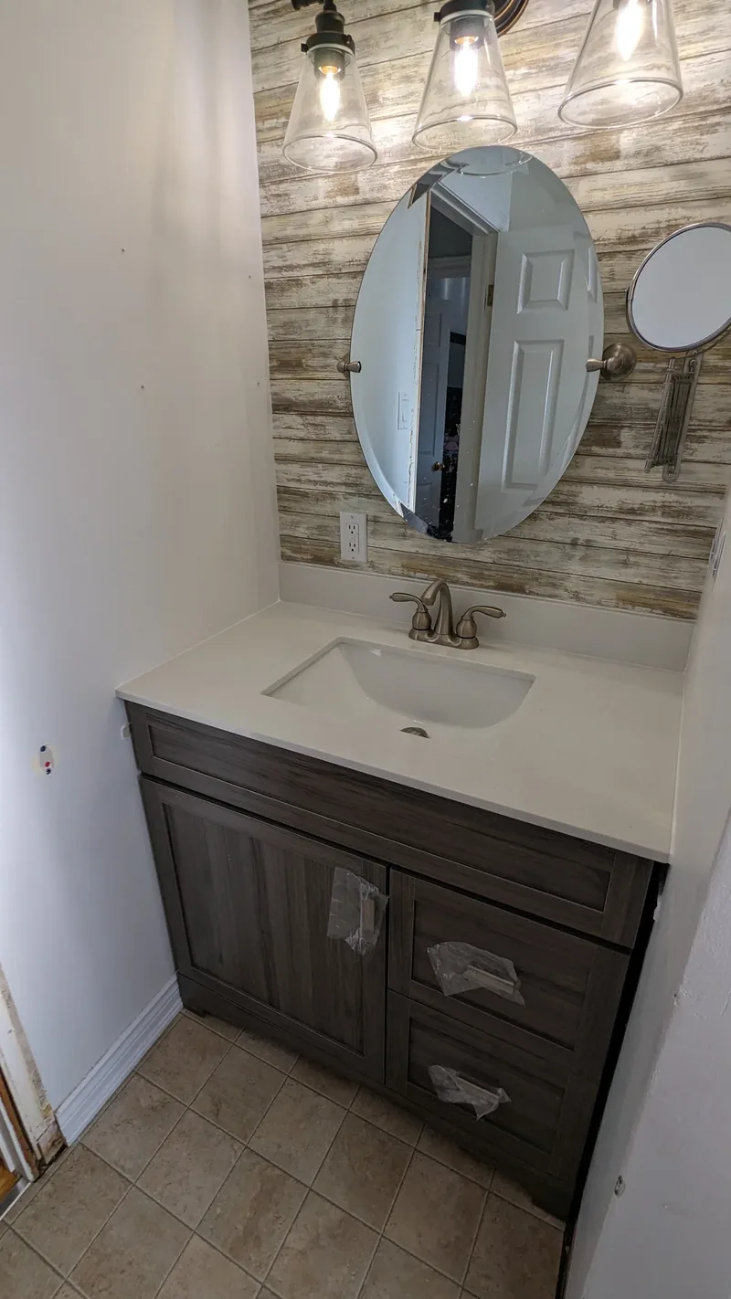 Bathroom vanity with a quartz top, oval pivot mirror, and a wood-plank feature wall