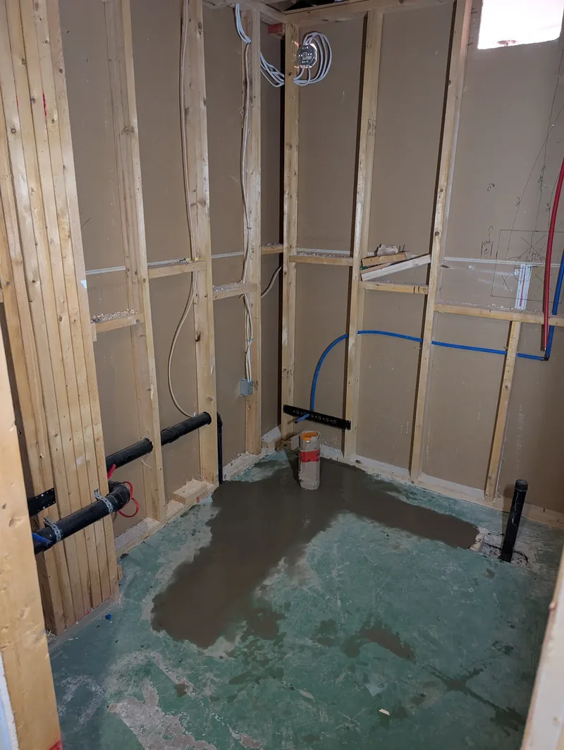 Bathroom rough-in with red and blue PEX supply lines and black ABS drain piping run through a stud wall