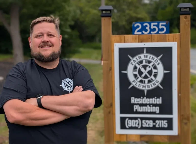 Clinton, owner of Fair Winds Plumbing, standing by his shop sign