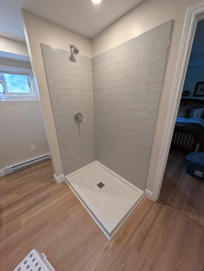 Finished tiled alcove shower with a glass partition and a hardwood floor