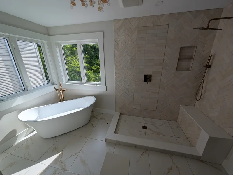 Renovated ensuite with a freestanding soaking tub and a walk-in herringbone tile shower with brushed bronze fixtures