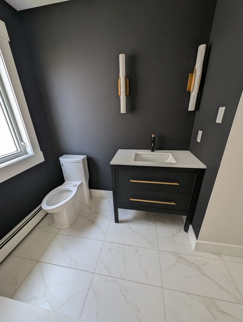 Powder room with charcoal walls, a black vanity with gold pulls, and a one-piece toilet