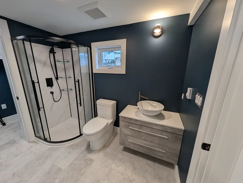 Basement bathroom with navy walls, a corner glass shower, and a floating vanity with a vessel sink