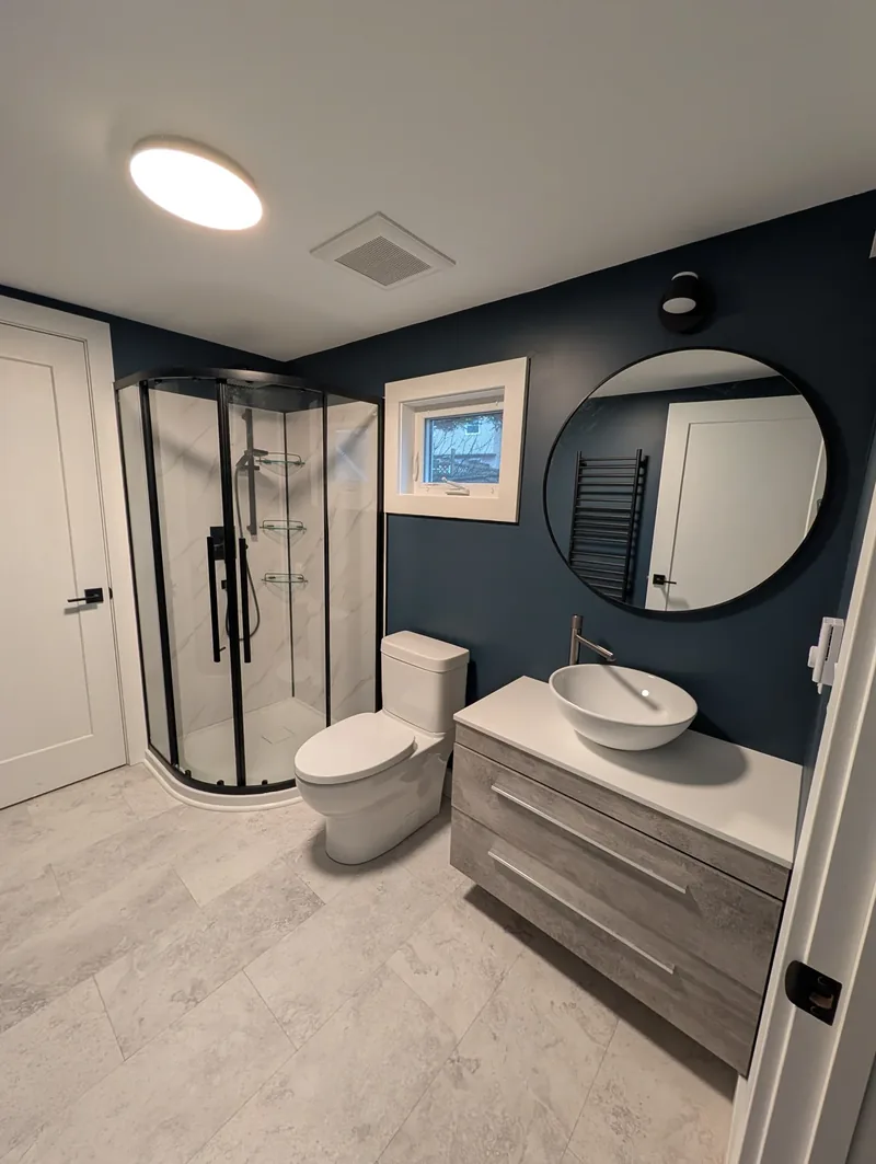Finished bathroom with navy walls, a round black mirror, and a floating vanity